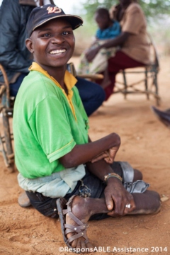 Another physically disabled man smiles at the camera while he sits on the floor