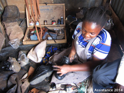 Margaret sits on the floor of her roadside shack surrounded by the tools and materials she uses to mend and clean people’s shoes
