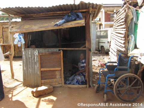 Margaret sits in the entrance of her shack, which is made from wood and corrugated iron sheets and in a poor state of repair