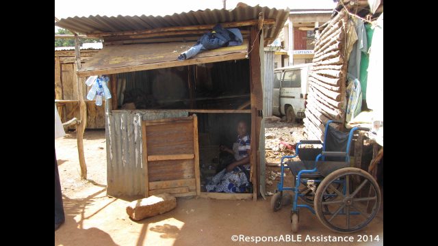 Margaret sits in the entrance of her shack, which is made from wood and corrugated iron sheets and in a poor state of repair