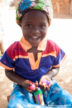 A little girl who happens to be deaf smiles with delight at a few small toys she has been given