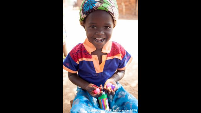A little girl who happens to be deaf smiles with delight at a few small toys she has been given