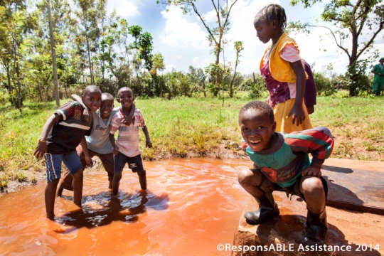 Five children playing and having fun in a puddle of overflow water