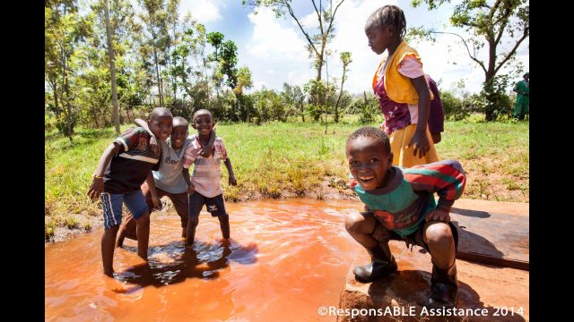 Five children playing and having fun in a puddle of overflow water