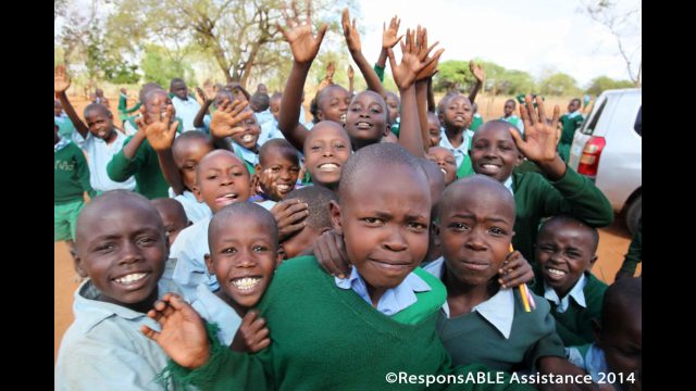 A group of children grinning and raising their hands while out in the school yard